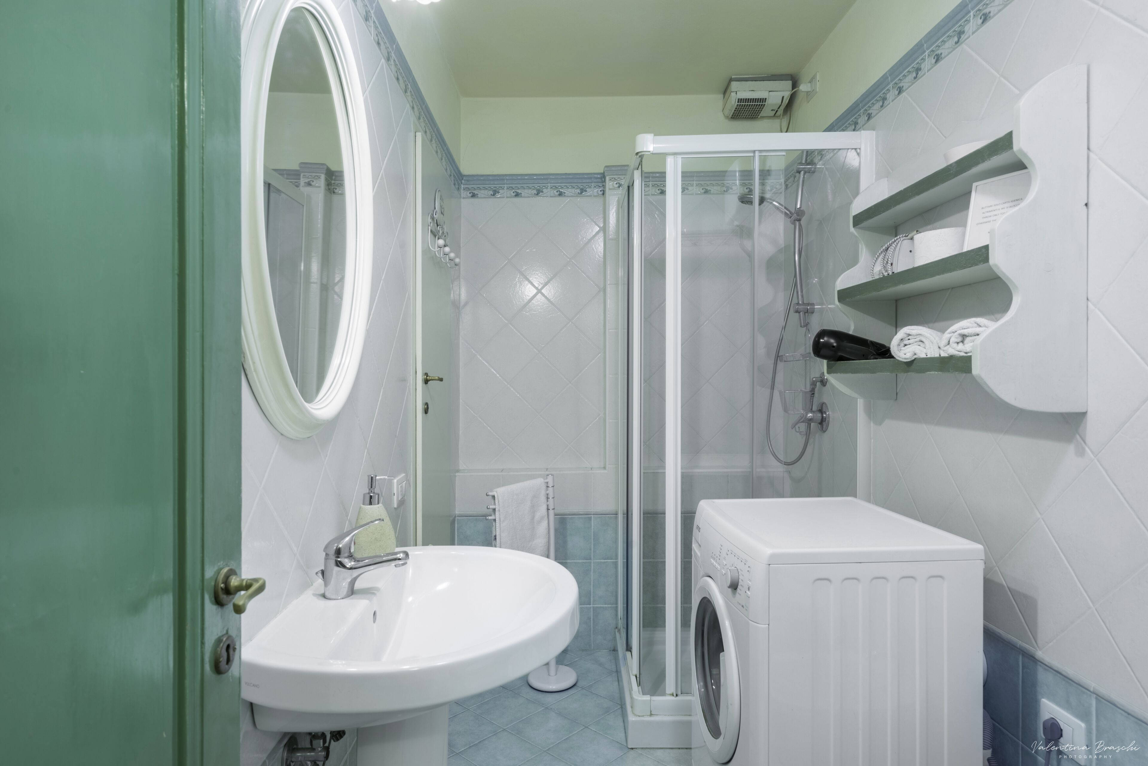 A bathroom with a sink, mirror, shower, and a washing machine.