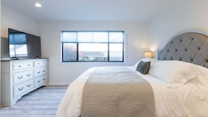 A bedroom with a bed, a dresser, a television, and a window with blinds.