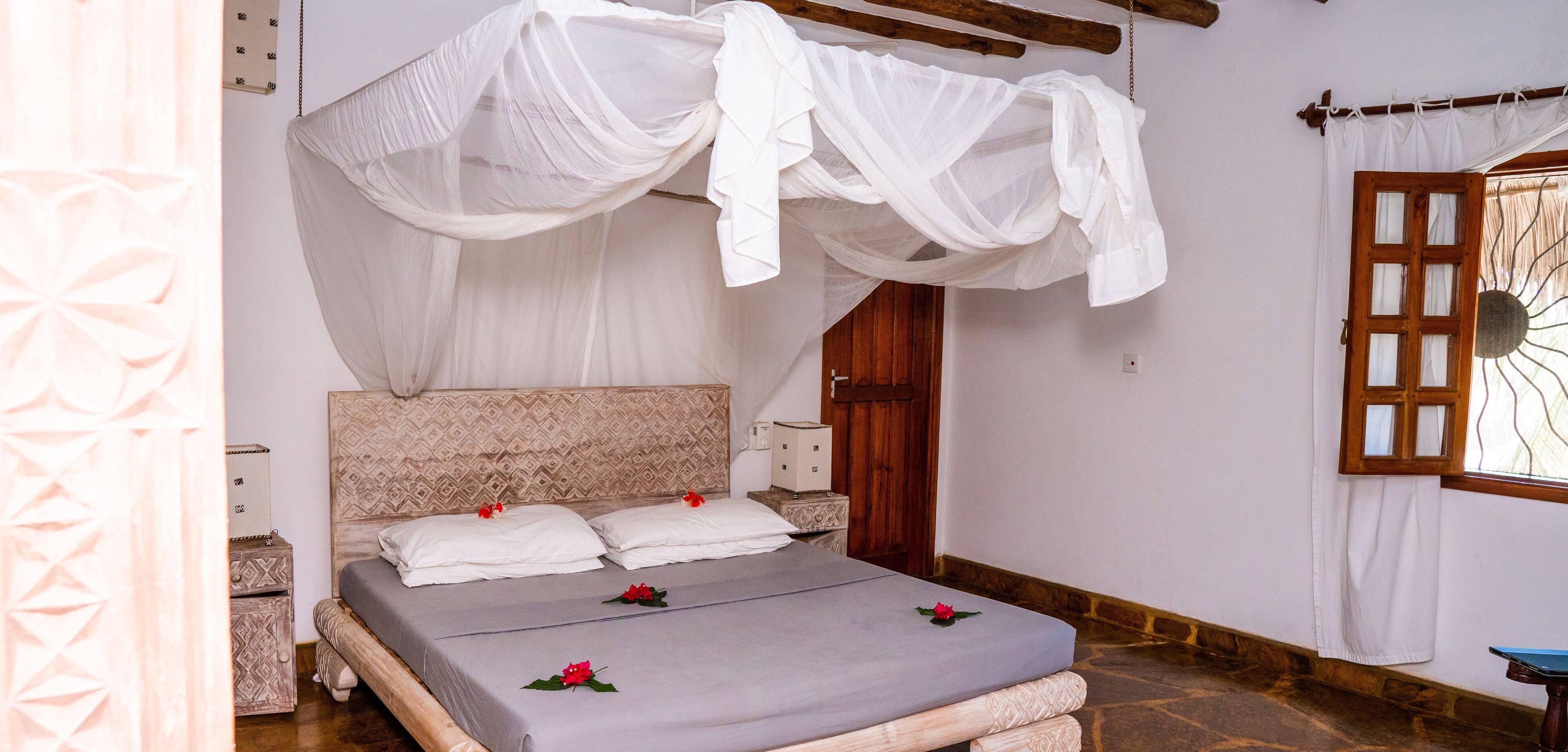 Una cama con dosel, una puerta de madera y un ventanal con celosía decorativa.