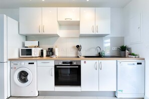 A modern kitchen with white cabinetry, a built-in oven, a dishwasher, a washing machine, and a microwave.