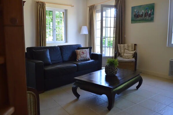 A living room with a dark-colored sofa, a wooden coffee table with a plant, and a chair with a cushion.