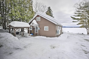 A cabin with a snow-covered roof, a porch, and a view of a lake.