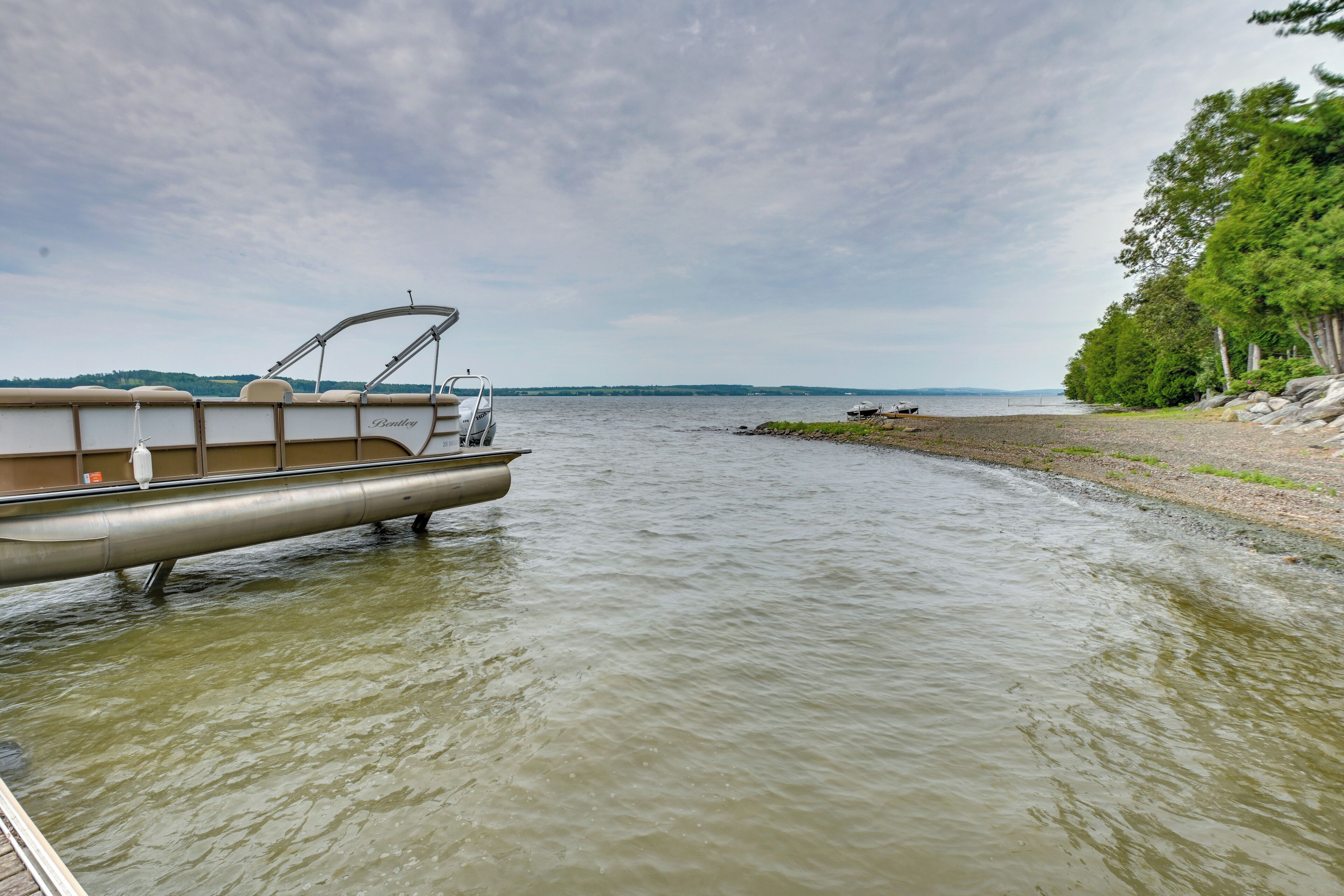 A pontoon boat docked at a lakeside with a view of the shoreline and trees.