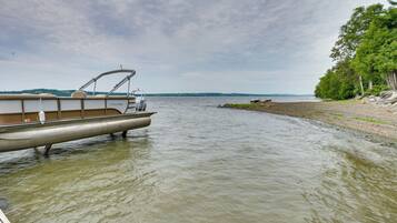 A pontoon boat docked at a lakeside with a view of the shoreline and trees.