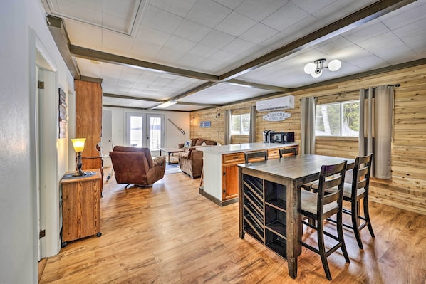 A spacious kitchen with a central island, wooden flooring, and a view of the outdoors through large windows.