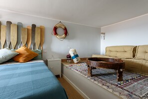 A bedroom with a bed, a sofa, a wooden table, a rug, and a wall-mounted life preserver. - Altre Stelle Suite Apartments: warm•soft design•cozy soul (Pozzuoli)