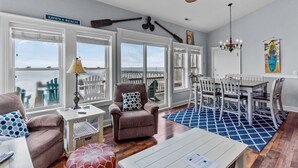 A spacious living area with large windows, a dining set, and a view of the ocean.