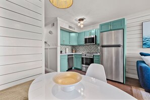 A modern kitchen with teal cabinets, stainless steel appliances, and a white dining table. - Freshly remodeled condo near the beach! (Galveston)