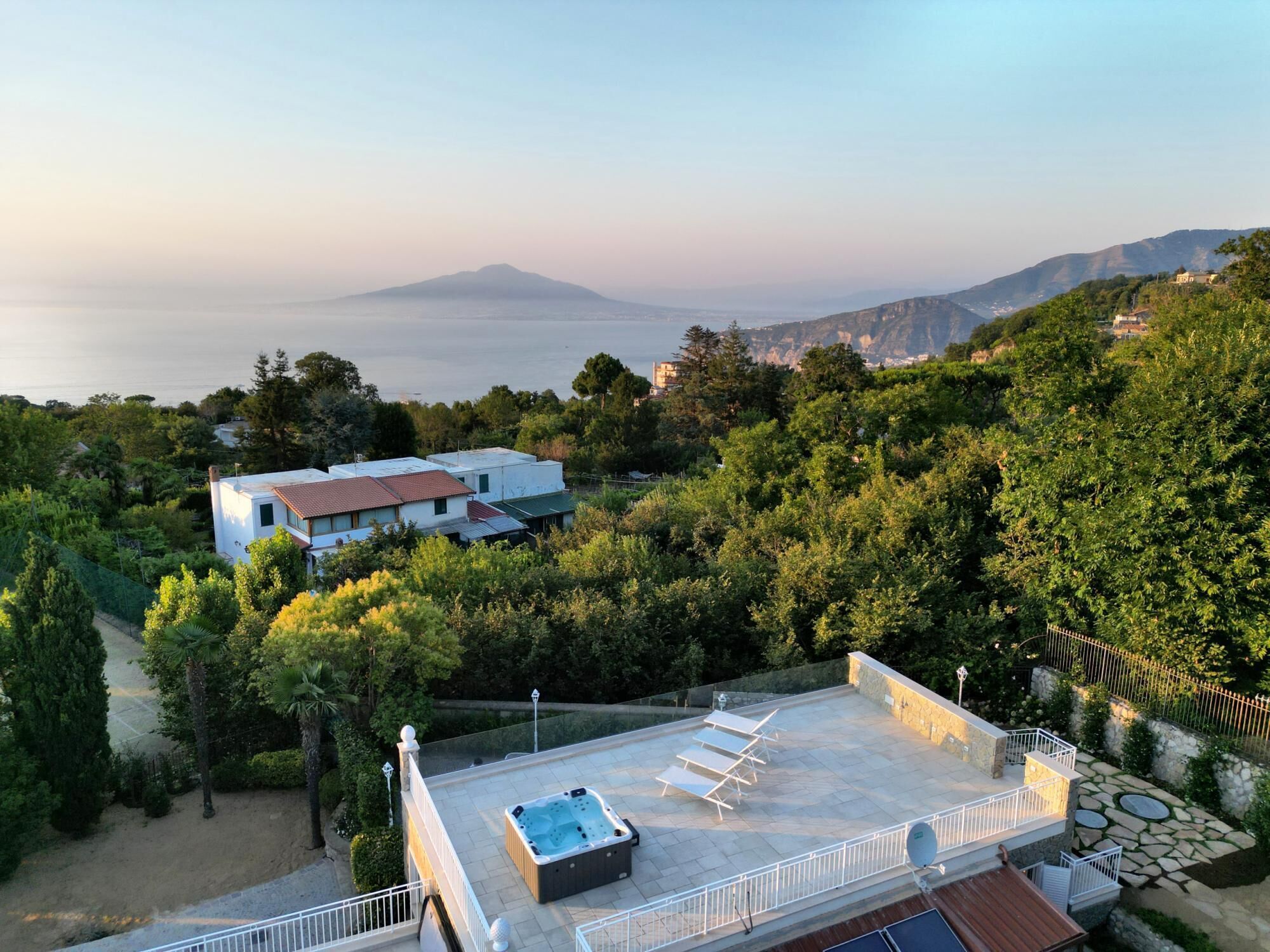 A rooftop with a hot tub, lounge chairs, and a view of the sea and mountains.