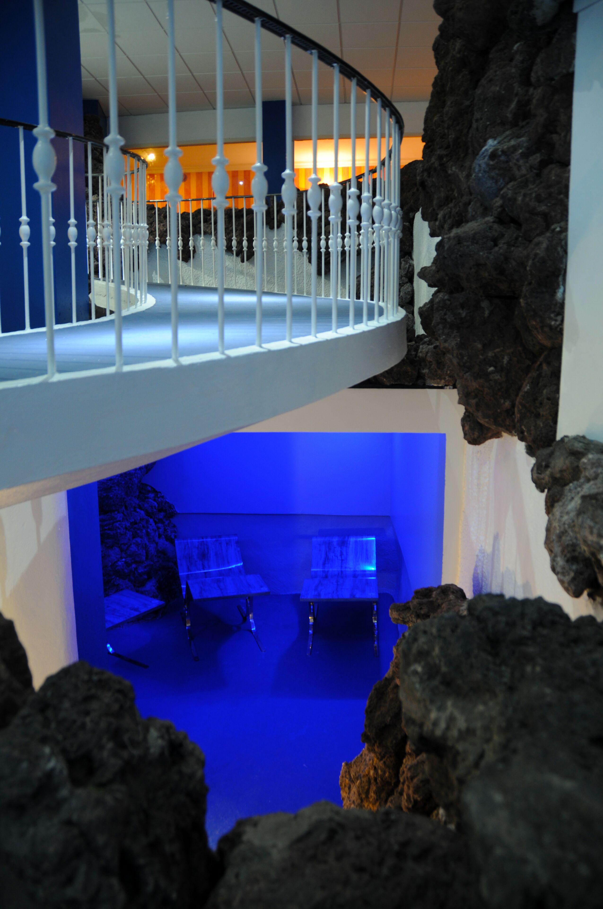 Un interior moderno con una escalera espiral, una zona de piscina con iluminación azul y un espacio para comer.