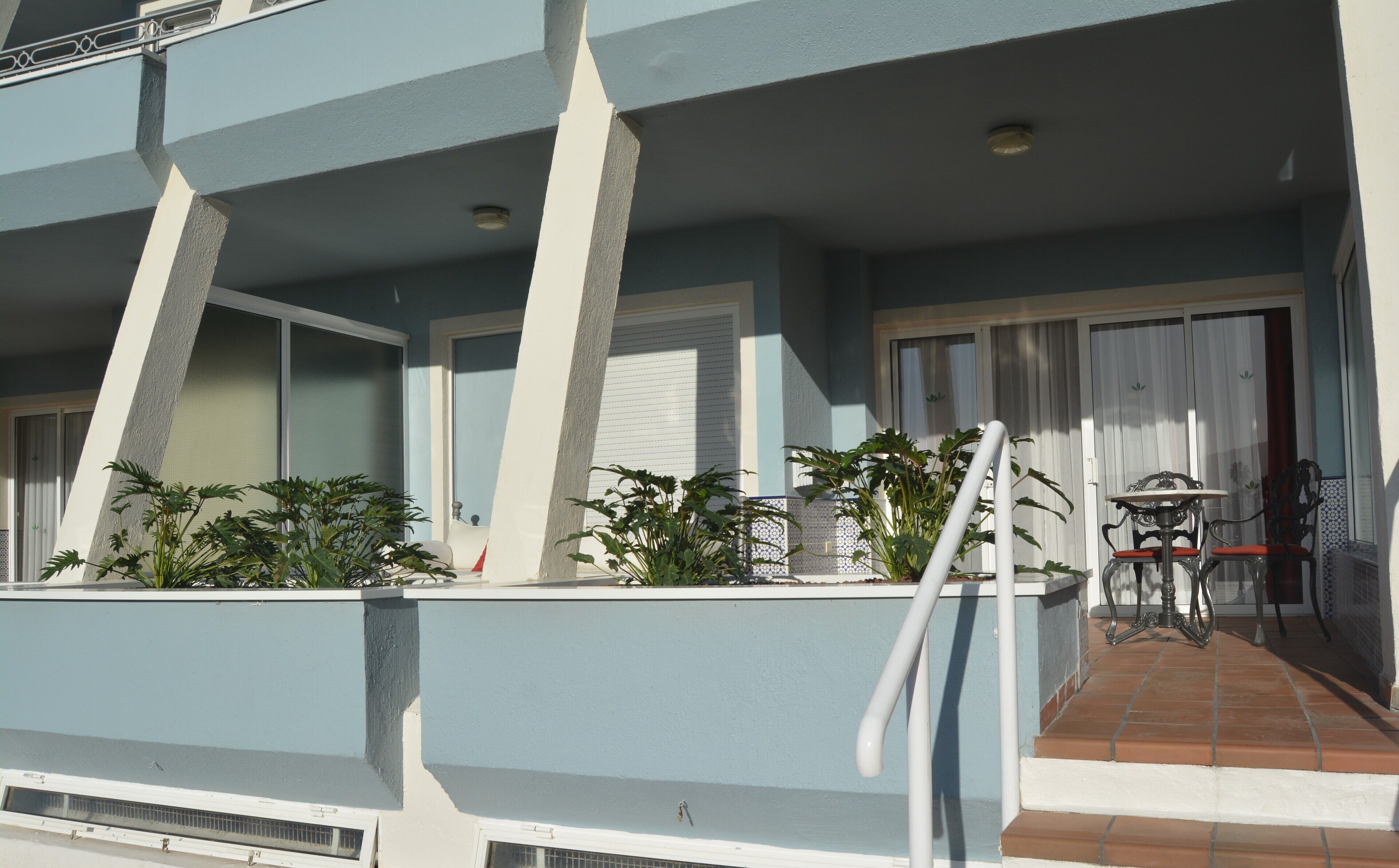 A multi-story building with balconies, outdoor seating, and potted plants.
