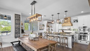 Een moderne keuken met een houten eettafel, hangende lampen en witte kastjes.