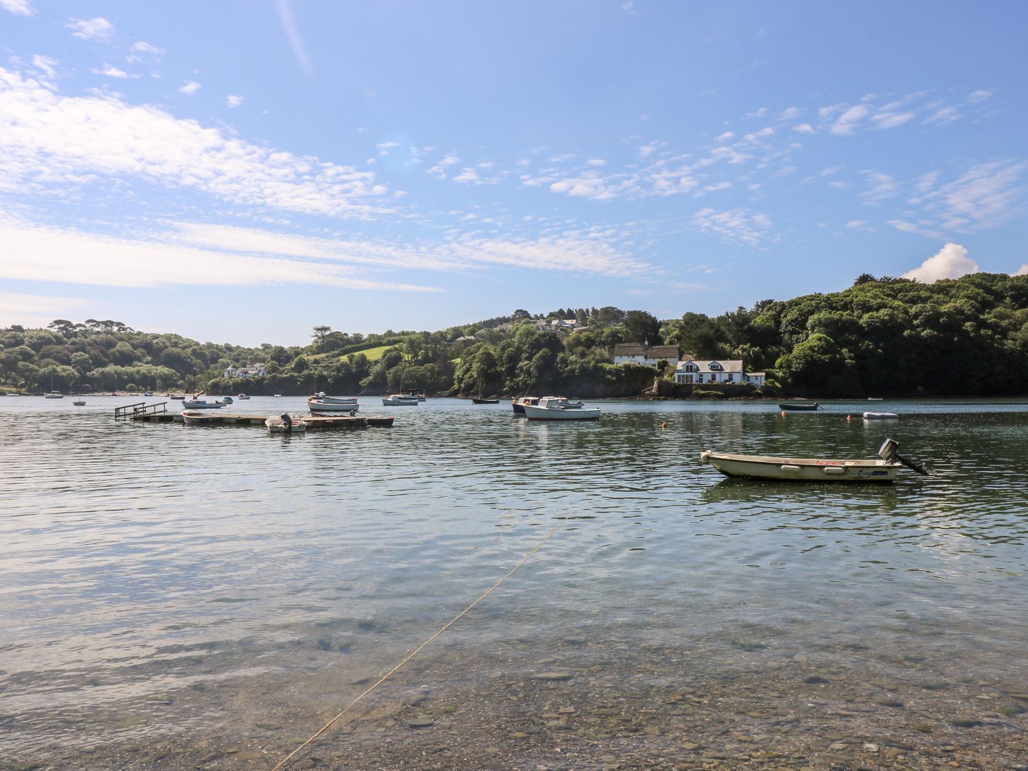 A calm lake with several boats docked, surrounded by lush greenery and a few houses.