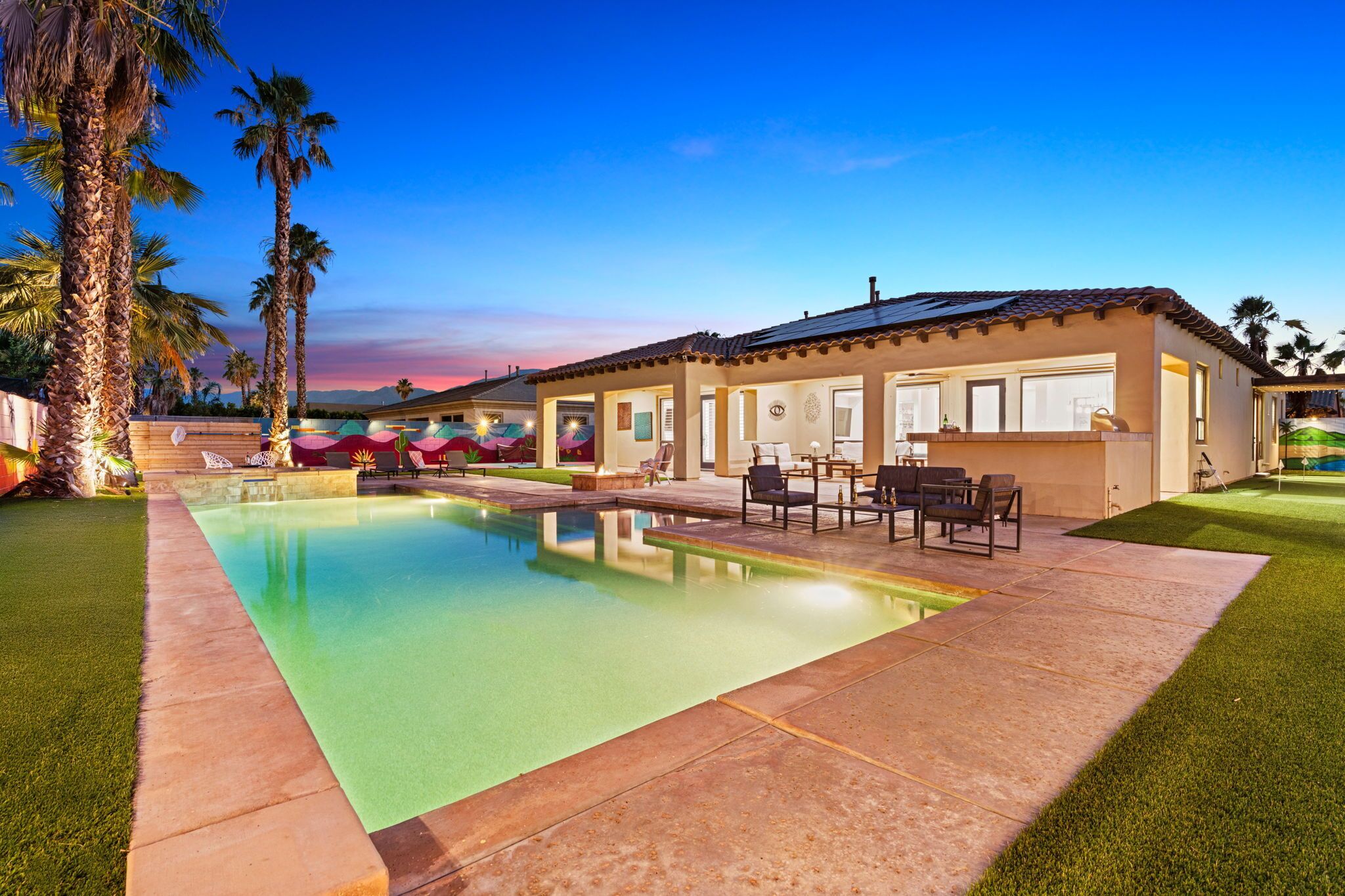 A swimming pool with a patio area, palm trees, and a building with a tiled roof.
