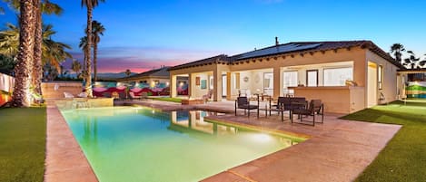A swimming pool with a patio area, palm trees, and a building with a tiled roof.