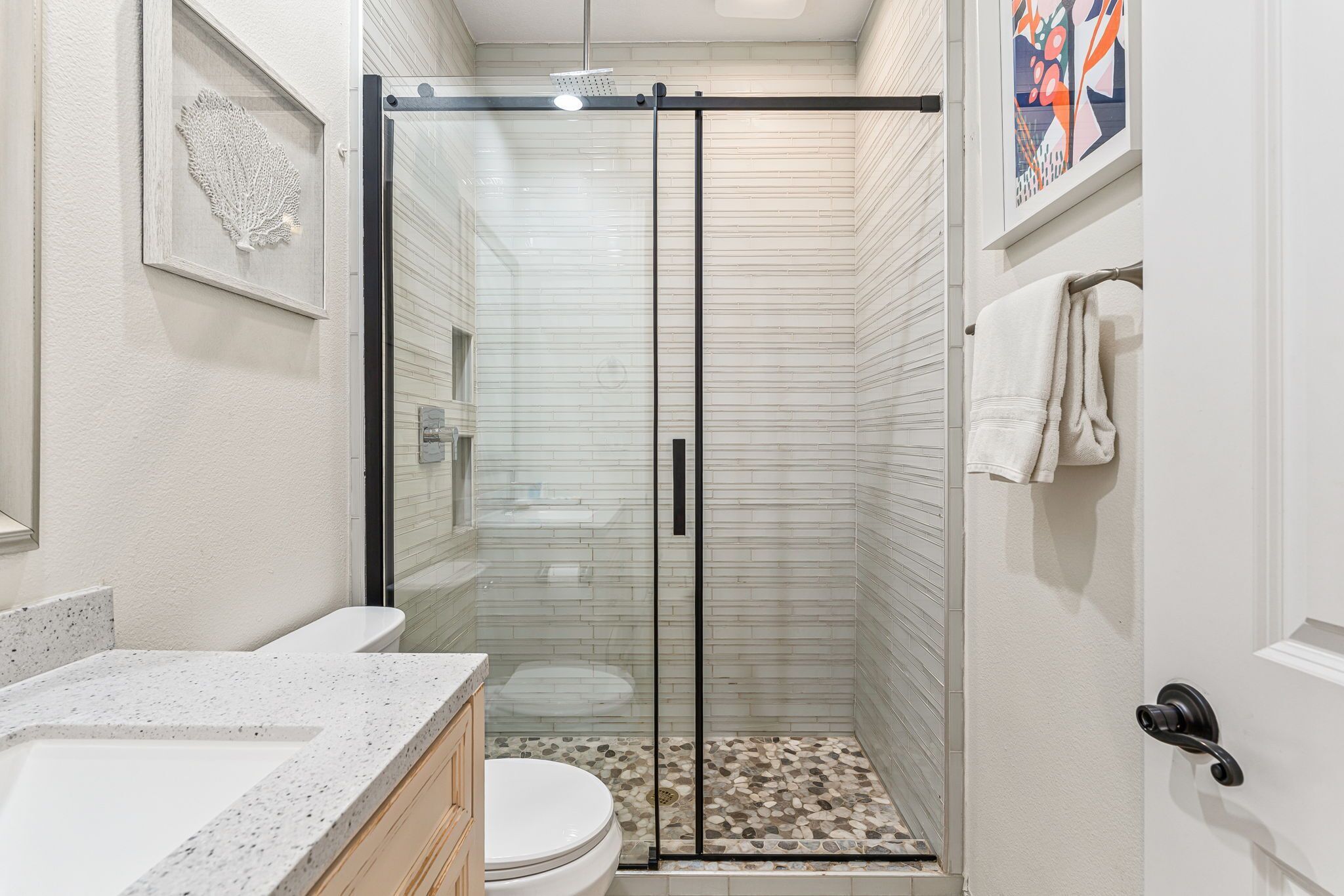 A modern bathroom with a glass shower enclosure, a toilet, and a sink with a speckled countertop.