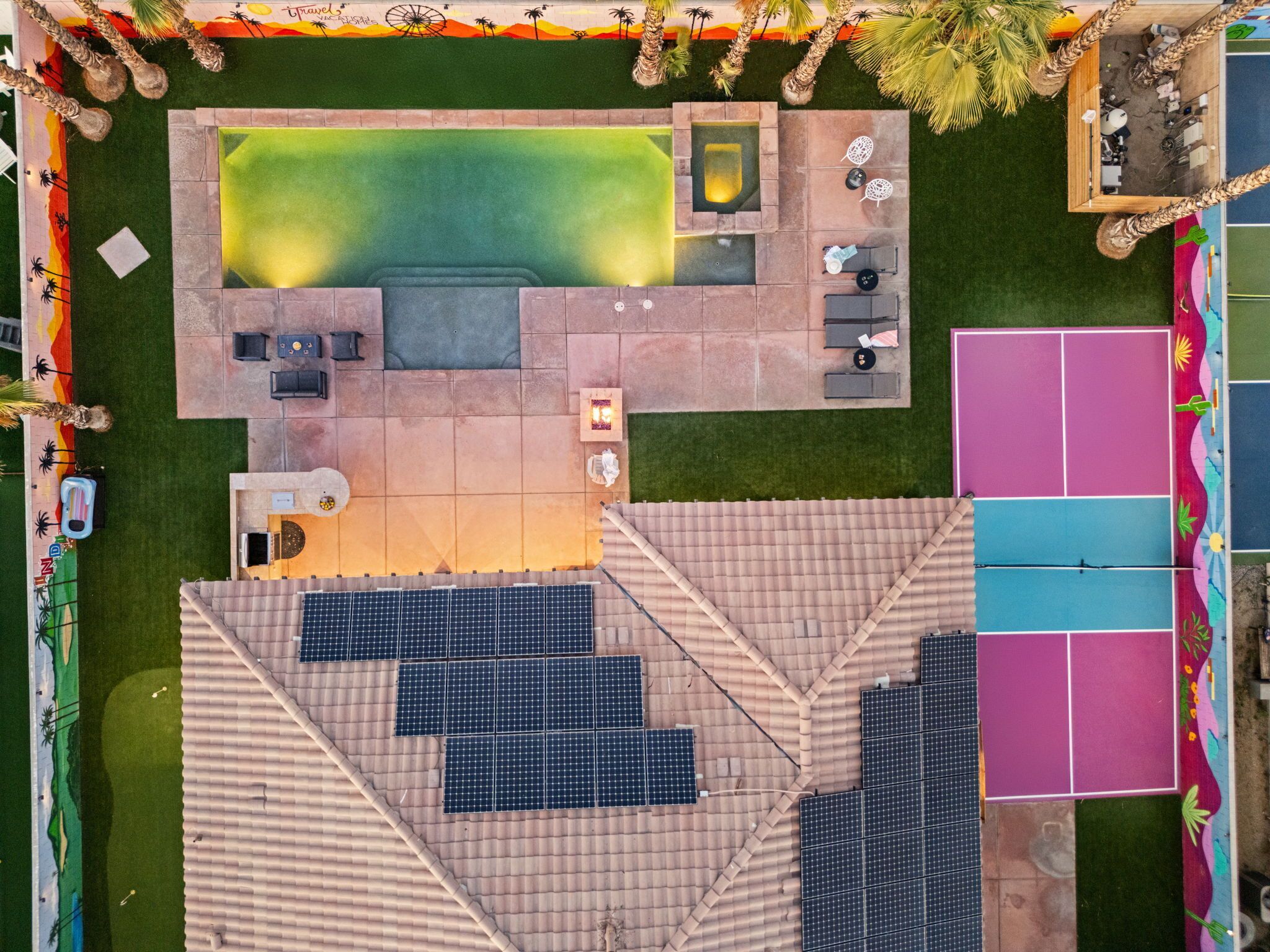 An aerial view of a resort with a swimming pool, outdoor seating, and a tennis court.