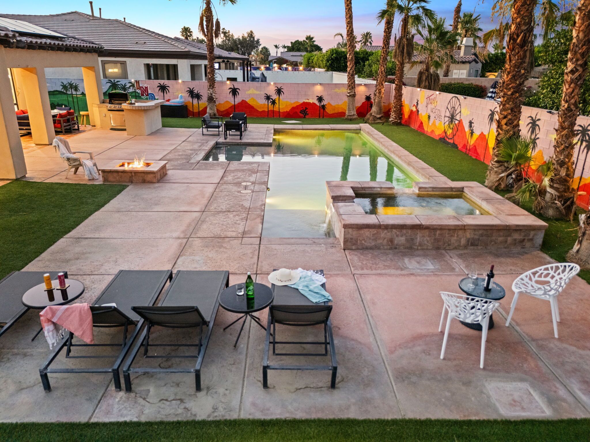 Un jardin avec une piscine, un espace salon extérieur et un mur décoré d’une fresque.