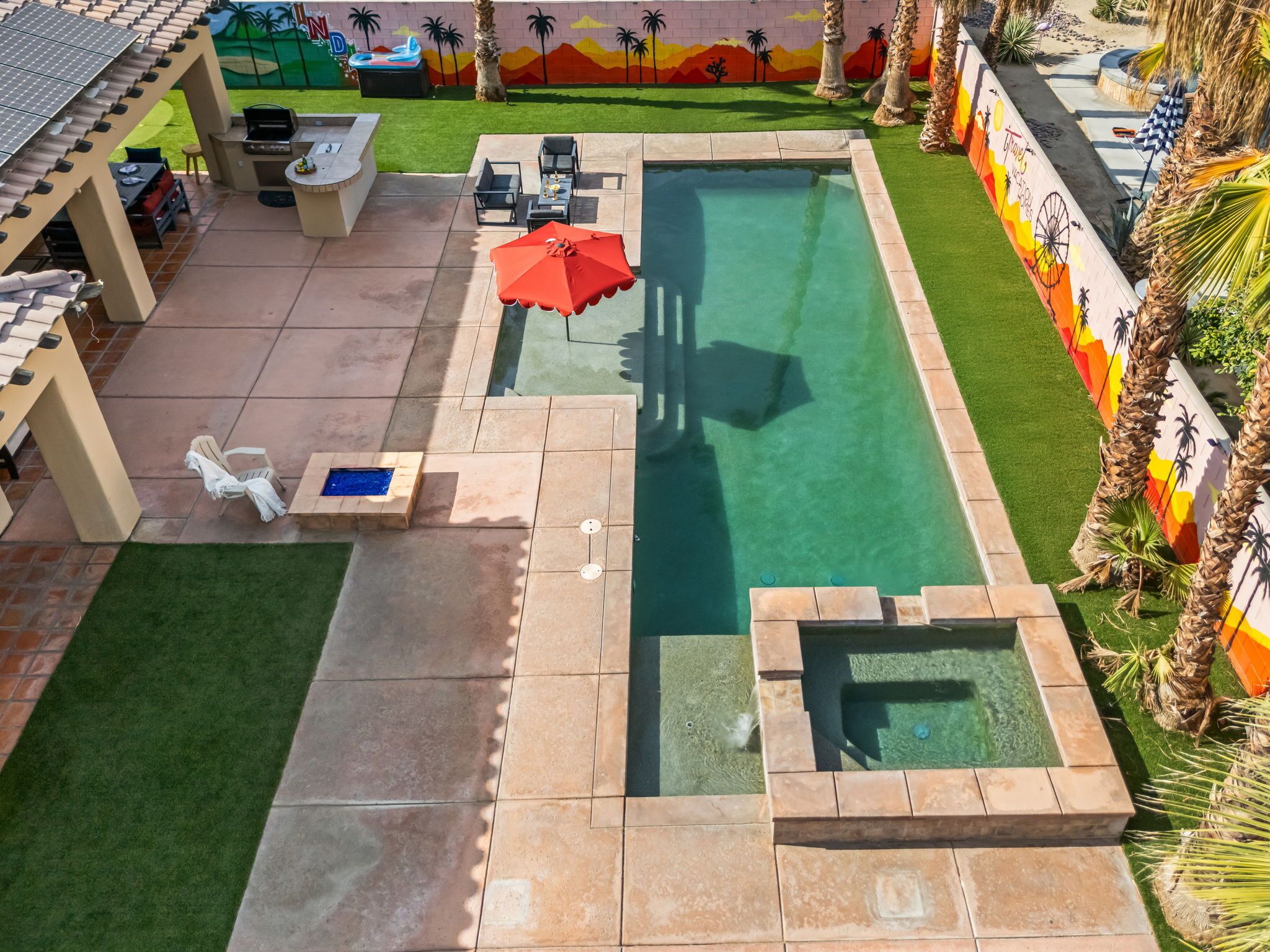 Zona de piscina exterior con área de barbacoa, sillas de descanso y un mural en la pared.