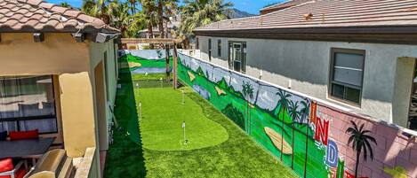 A courtyard with artificial grass, a mural, and palm trees.
