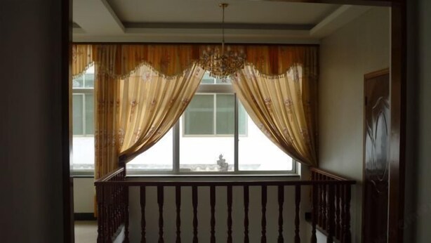 A room with a wooden railing, a chandelier, and a view through a window with curtains. - Jiakelong Hotel (Wuyuan)