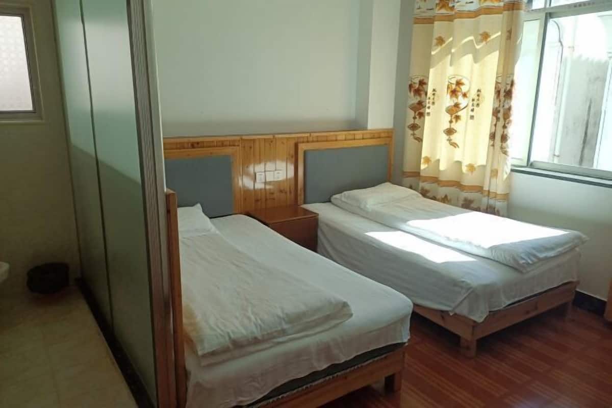 A room with two single beds, wooden headboards, a window with curtains, and a tiled floor.