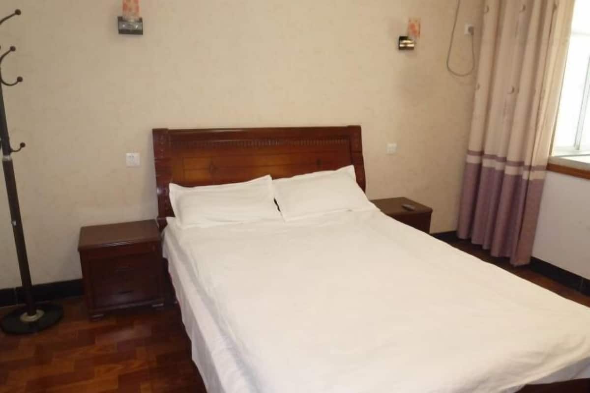A neatly made bed with white linens in a room with a wooden headboard, a small bedside table, and a floor lamp.