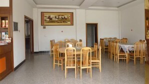 A dining area with round tables and wooden chairs, a painting on the wall, and a wooden counter with items on it. - Jiakelong Hotel (Wuyuan)