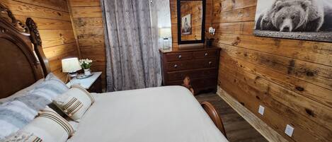 Ein Schlafzimmer mit Holzwänden, einem Bett, einer Kommode, einem Spiegel und einem an der Wand hängenden Bild.