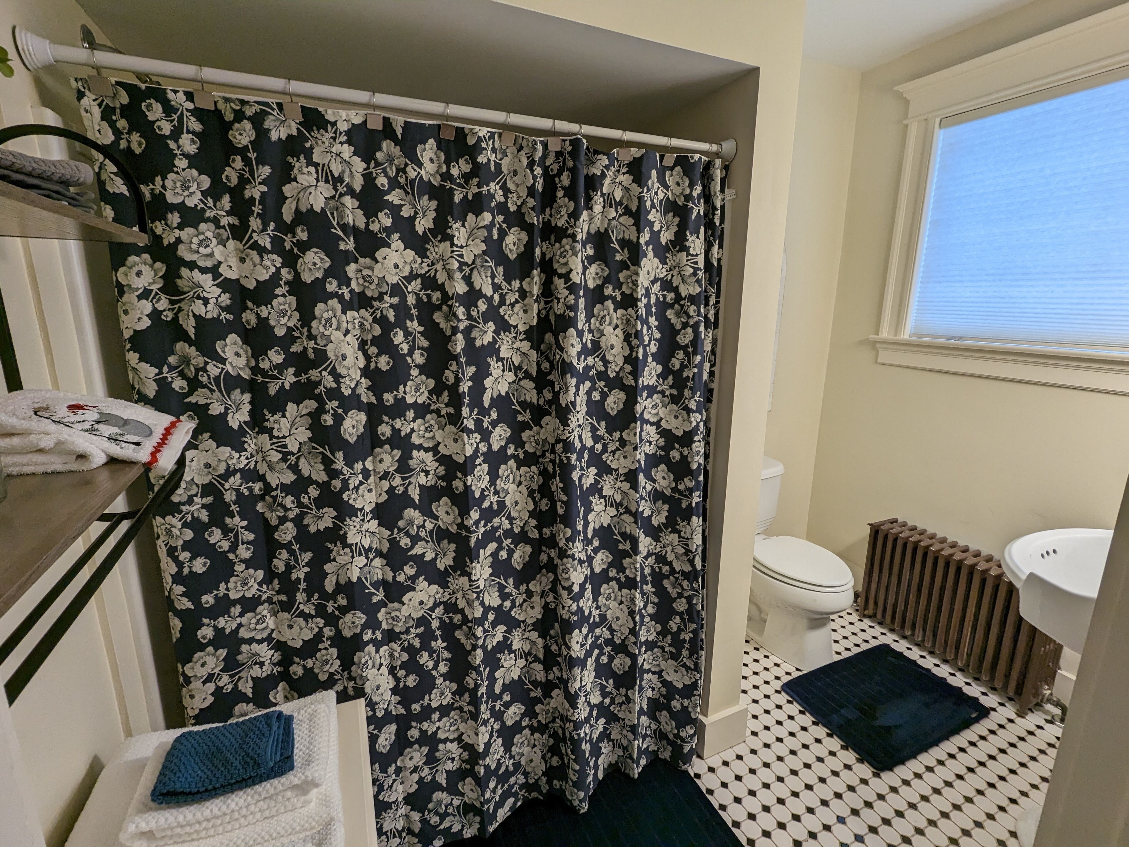A bathroom with a floral shower curtain, a toilet, a radiator, and a sink.