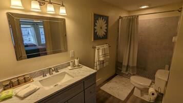 A bathroom with a large mirror, a sink with a marble countertop, a shower with a curtain, and a toilet.