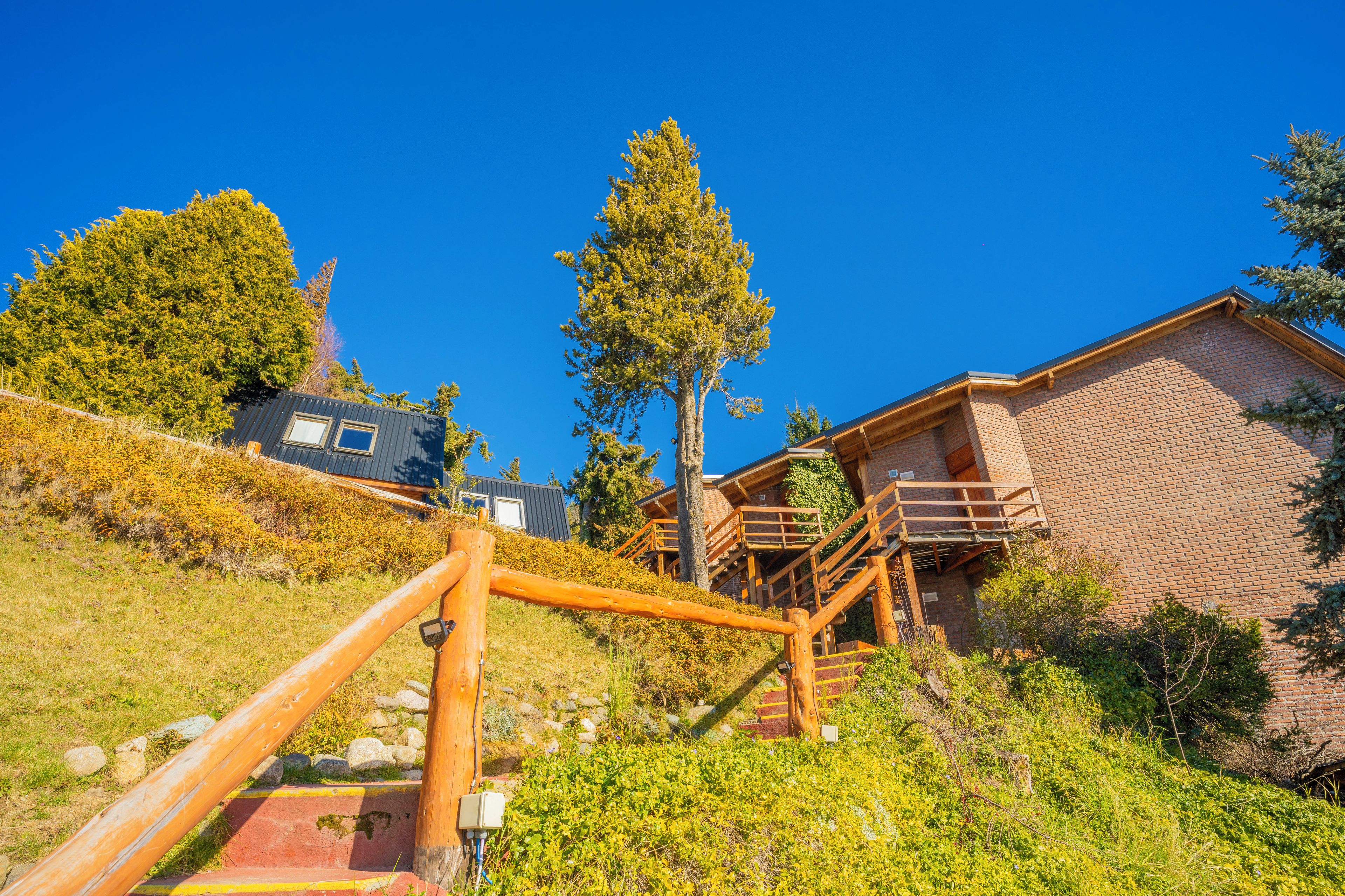 A wooden staircase leading to a brick building with a wooden deck and a metal structure in the background.