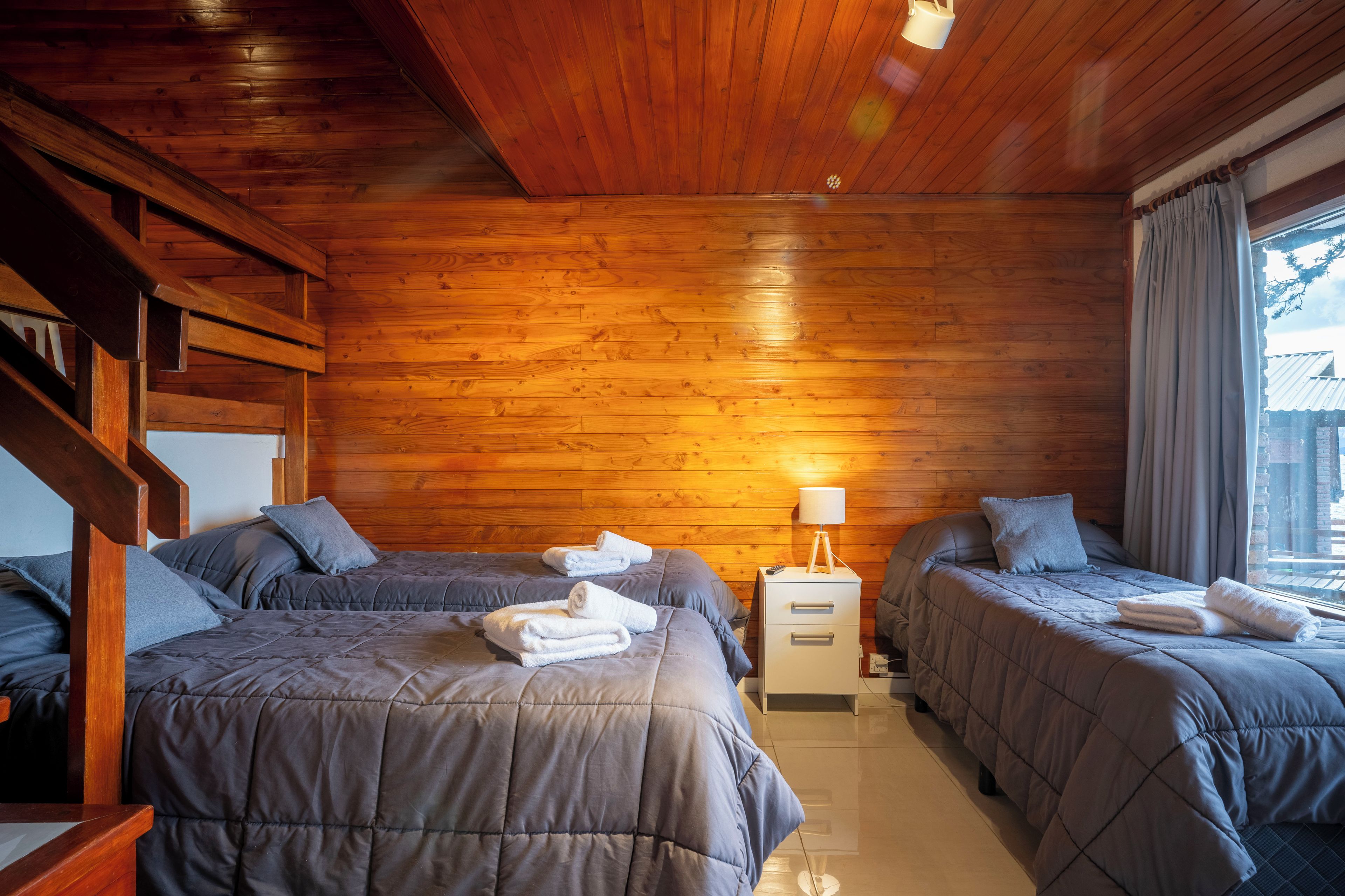 A hotel room with two beds, a nightstand, a lamp, and a window with curtains.