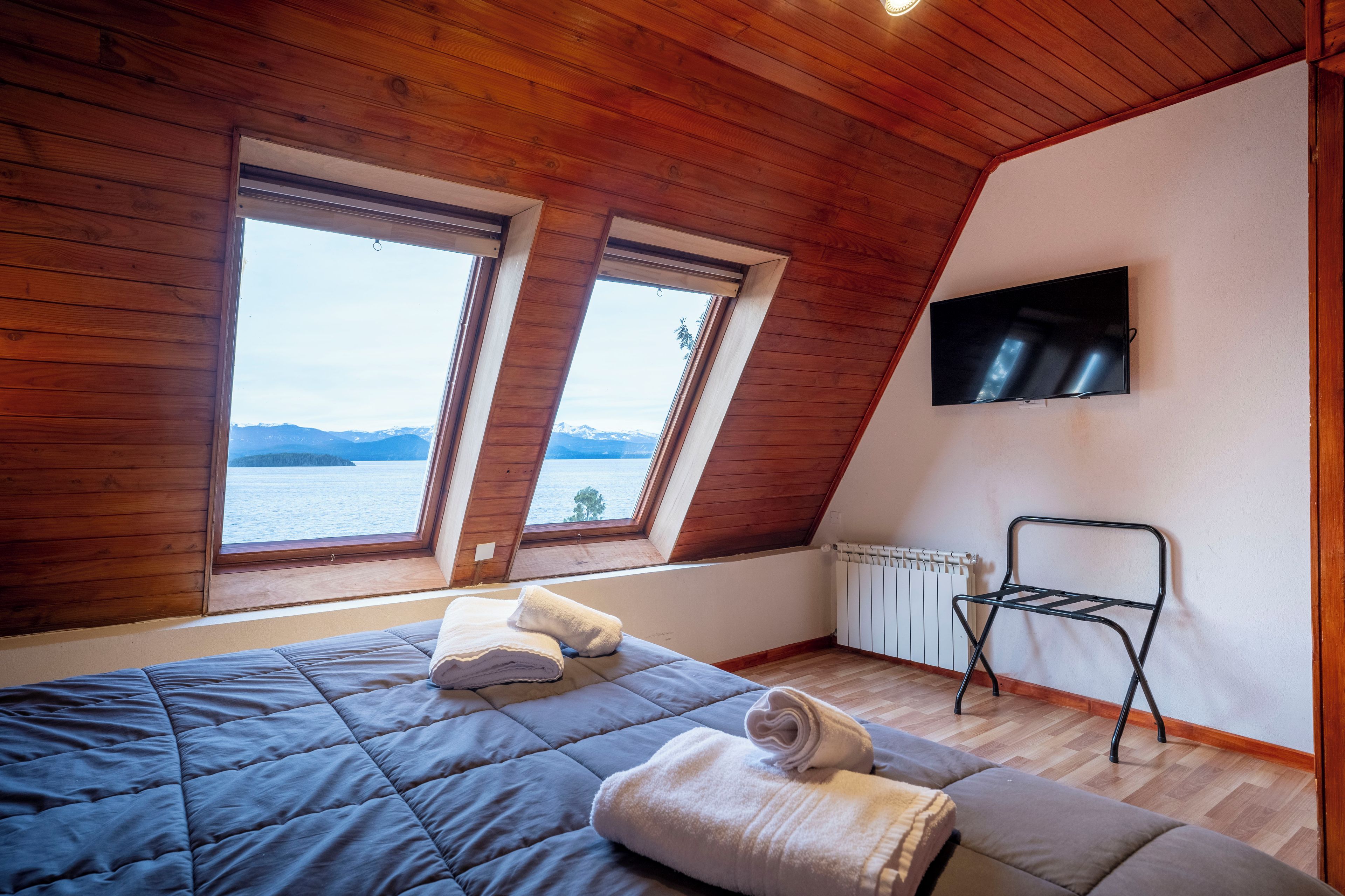 A bedroom with a bed, two windows, a radiator, and a TV.