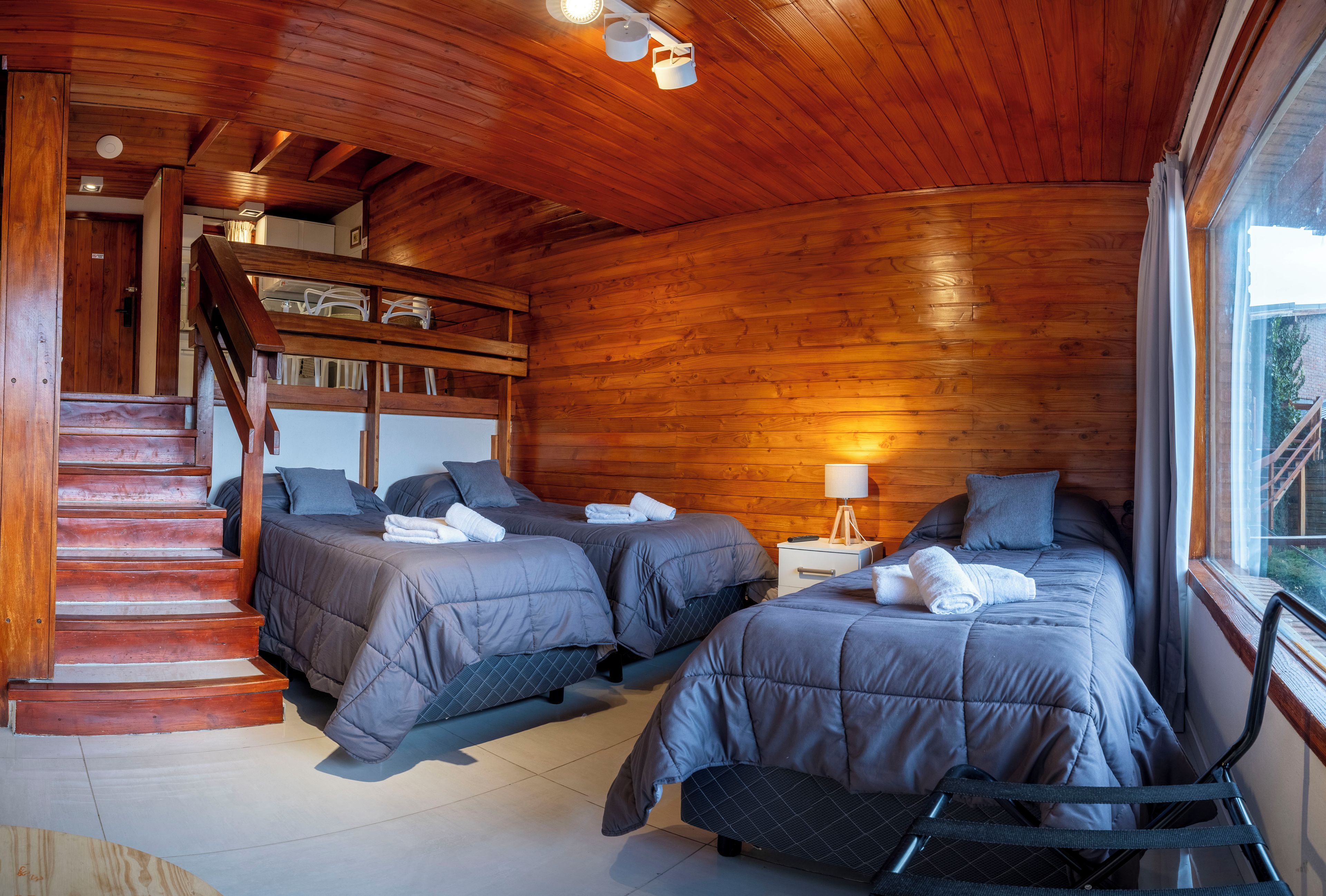 A room with two beds, a wooden staircase, and a window.