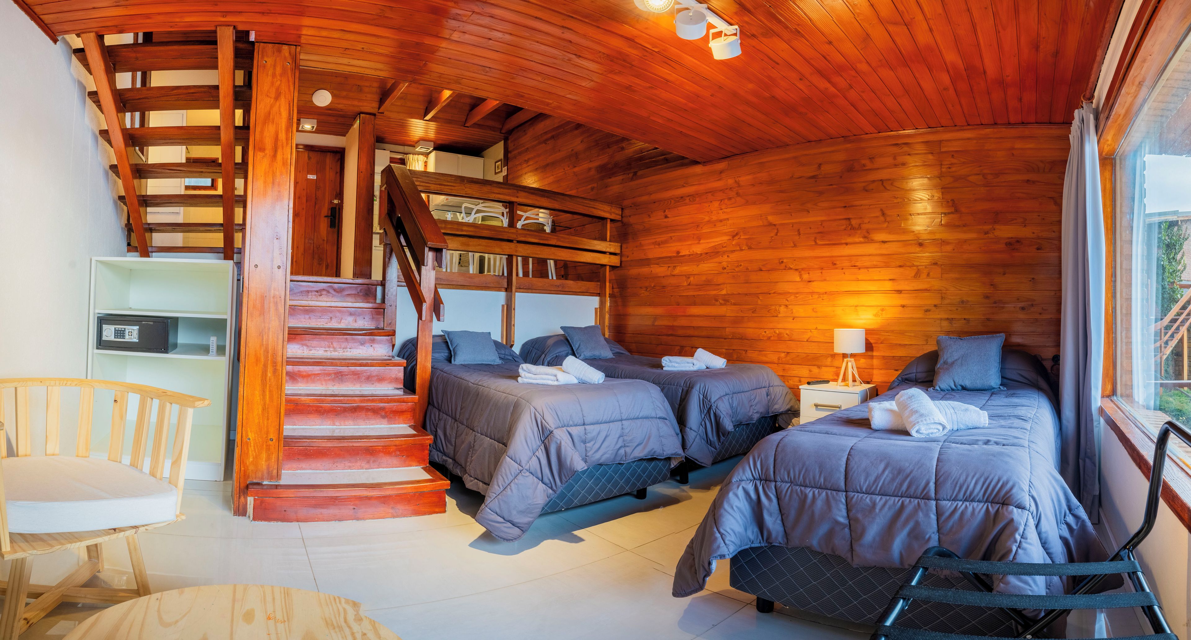 A wooden cabin with two beds, a staircase, and a small seating area.