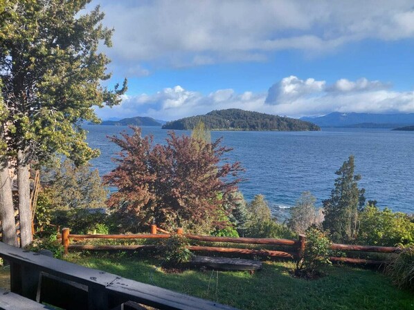 Vista de un lago con muelle de madera, árboles y una isla distante.