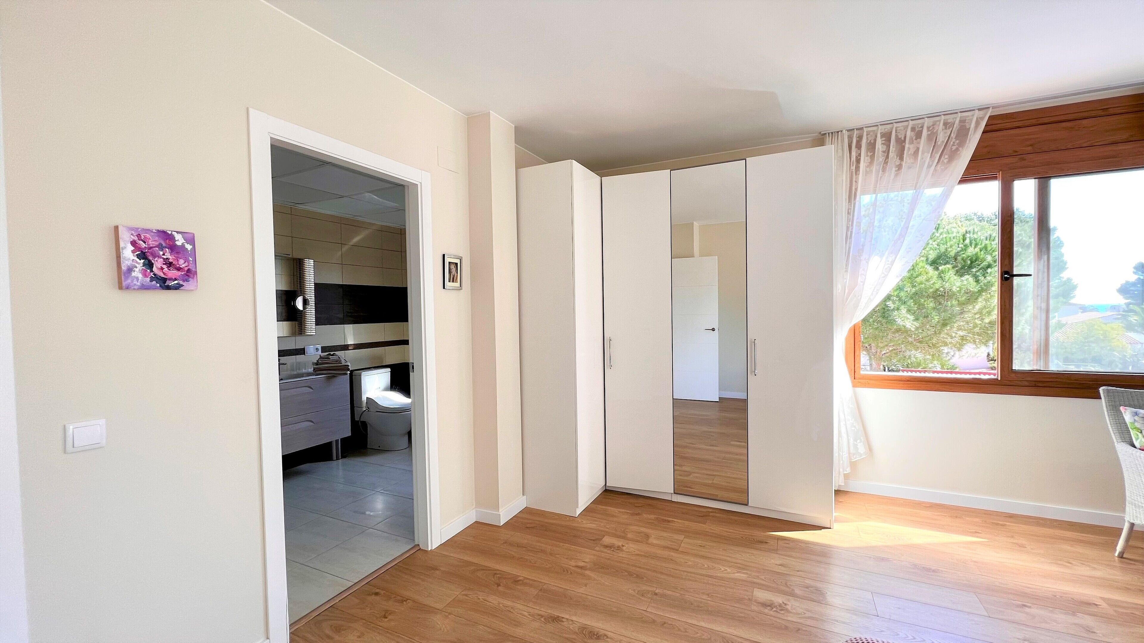 A modern kitchen with a refrigerator, sink, and cabinets. There is a wooden floor and a window with a view of trees.