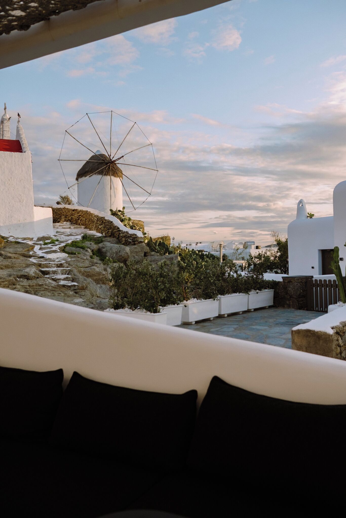 A coastal view with a windmill, white buildings, and a stone pathway.