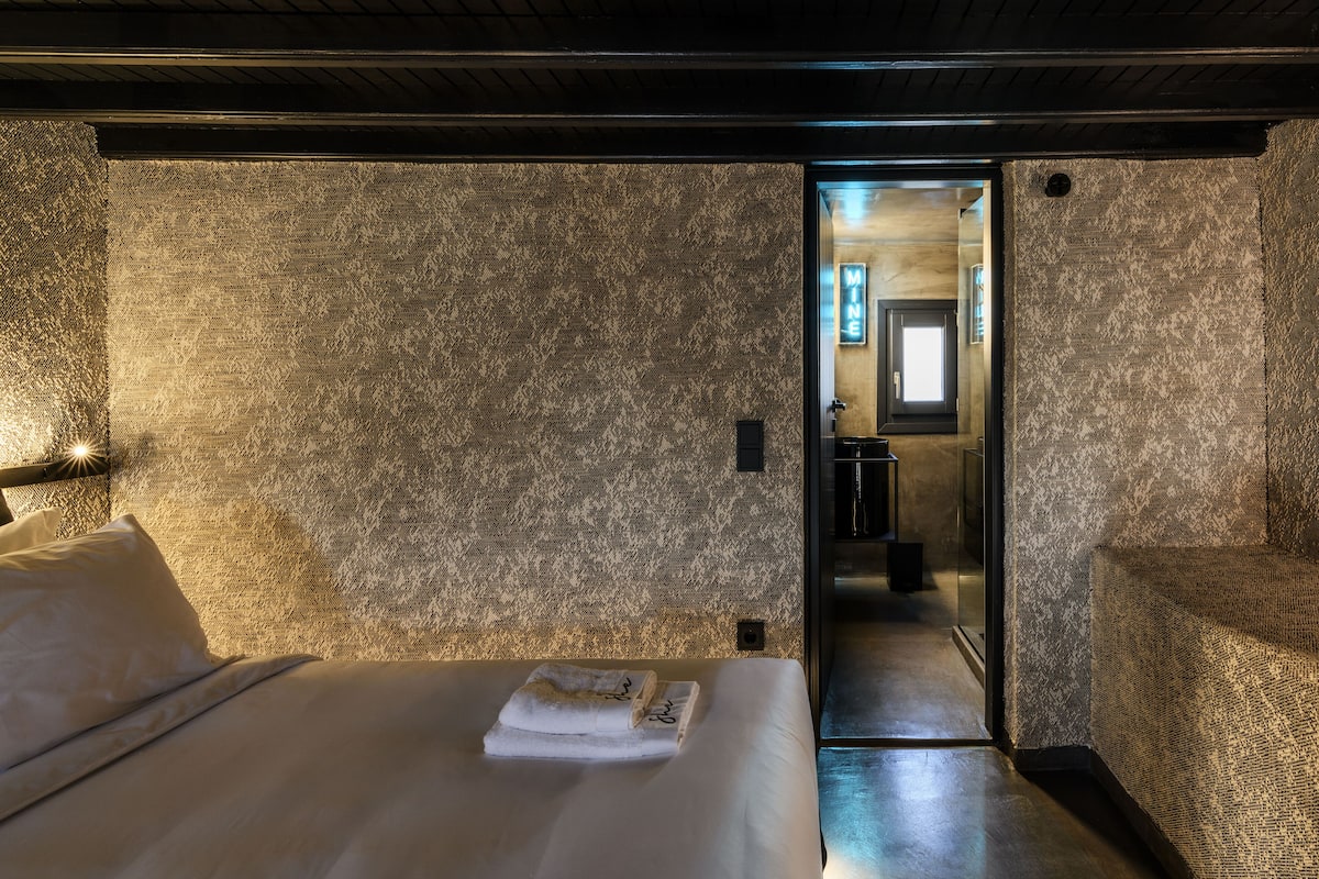 A hotel room with a textured wall, a neatly made bed with a towel, and a doorway leading to a bathroom.