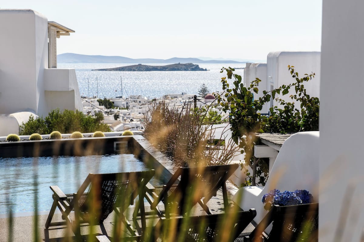 A poolside area with lounge chairs and a view of the sea and distant land.