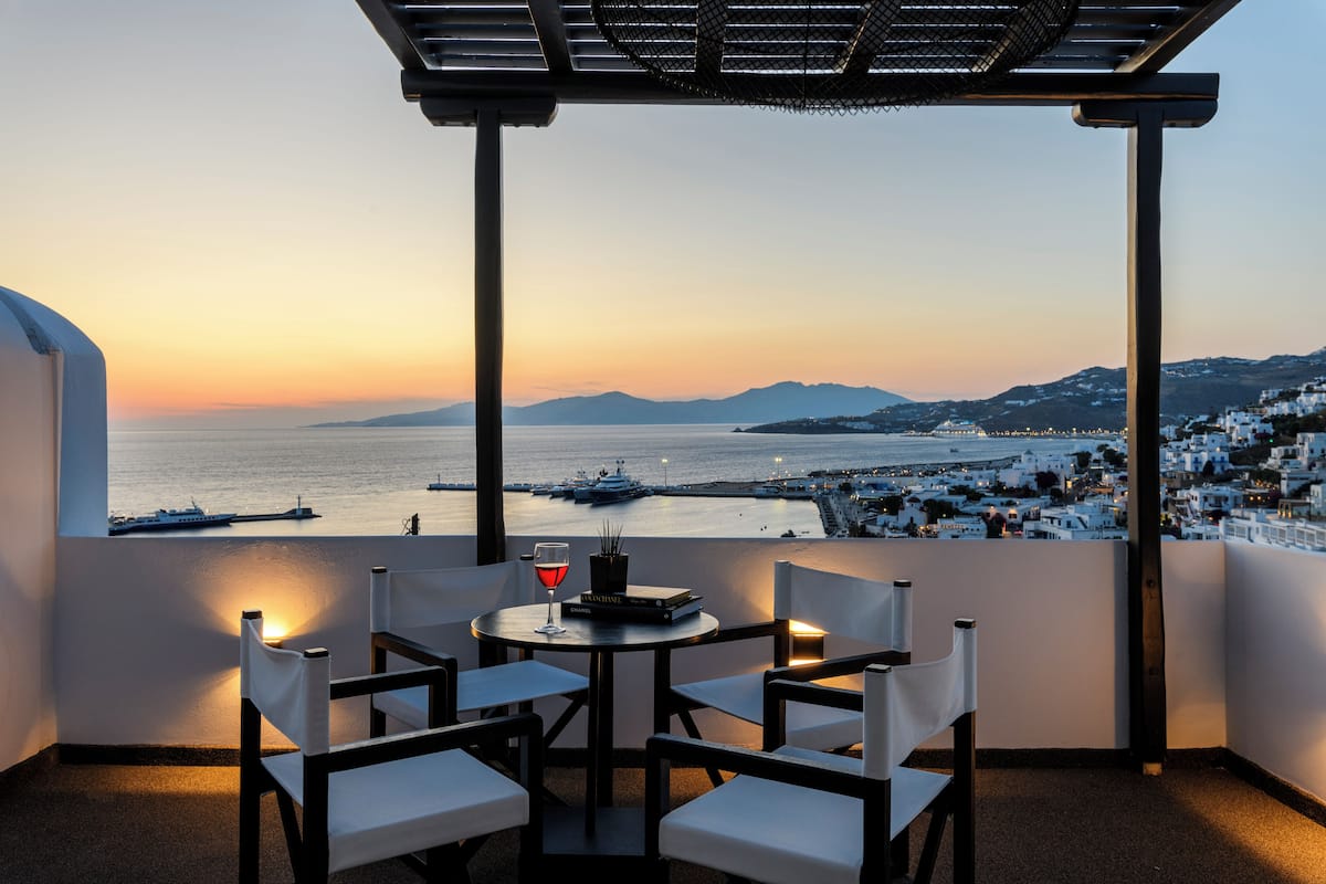 A terrace with a table and chairs, overlooking a coastal town at sunset.