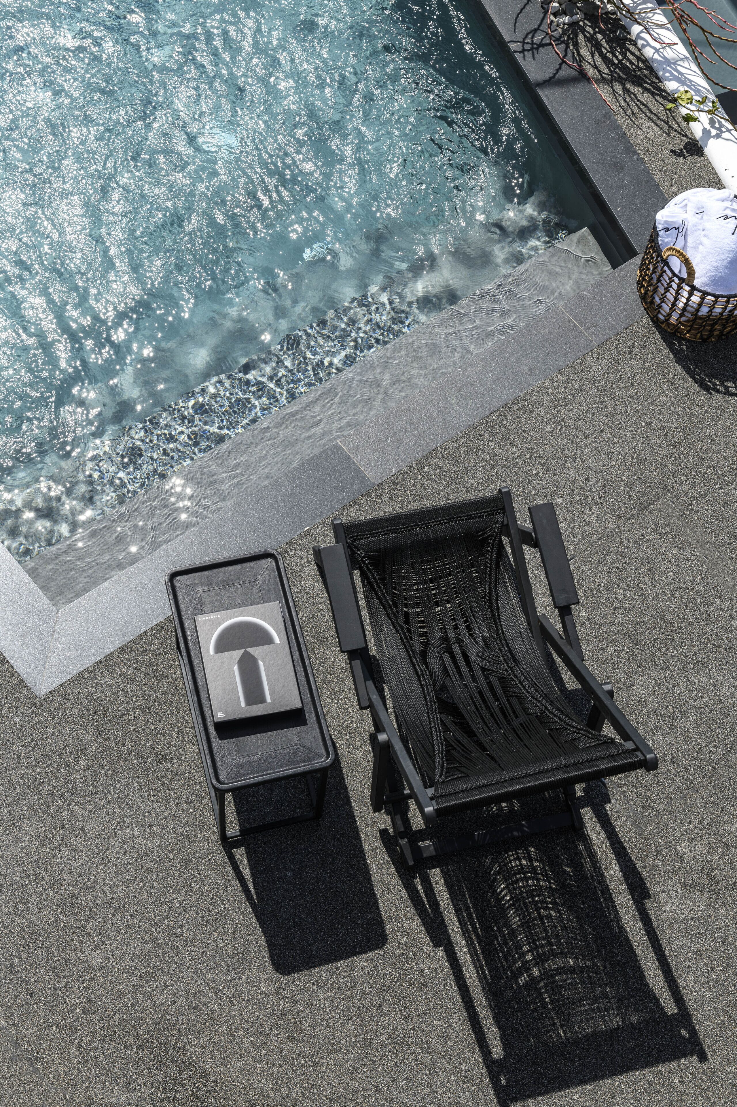 Zona de piscina con una silla de descanso y una mesita, rodeada por un borde de piedra.