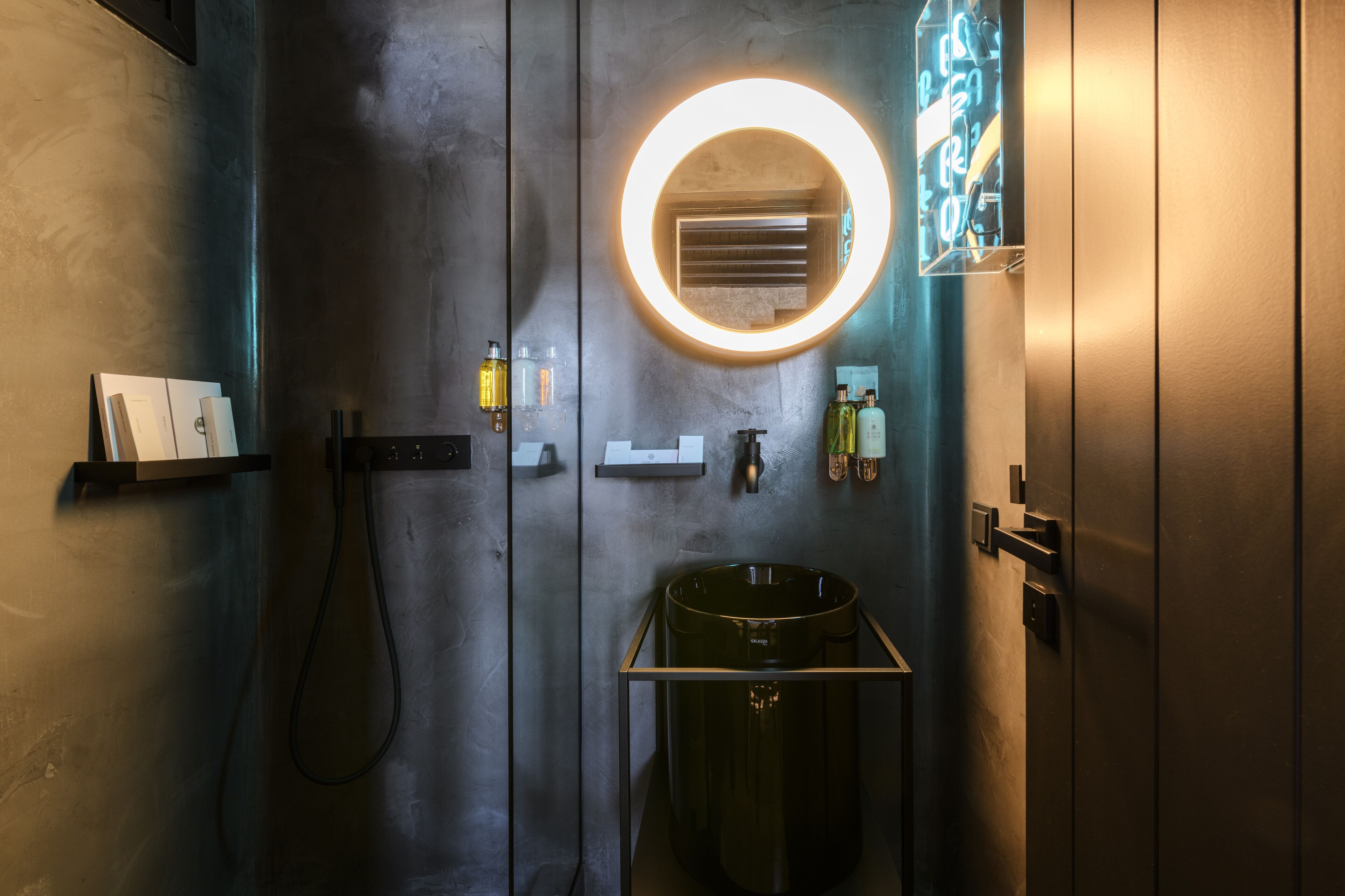 A modern bathroom with a large mirror, a round light fixture, a sink, and a towel rack.