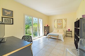 Quarto com cama, escrivaninha e cadeira. Porta de vidro deslizante dá acesso a uma varanda.