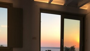 A bedroom with a bed, a window, and a view of the sunset. - She Mykonos - The Residency (Mykonos)