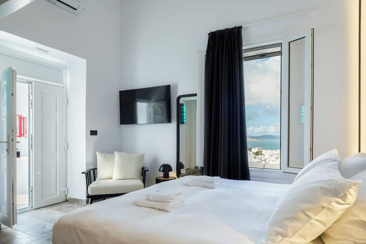 Una habitación de hotel con una cama, una silla, un televisor y vista al mar.