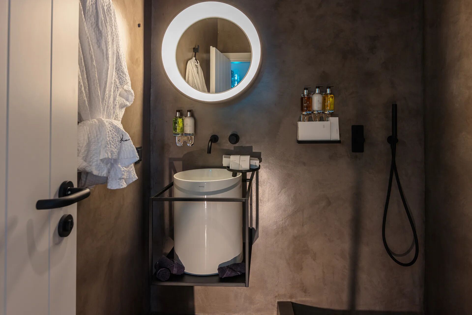 Une salle de bain moderne avec un miroir rond, un lavabo blanc et deux flacons de savon liquide.
