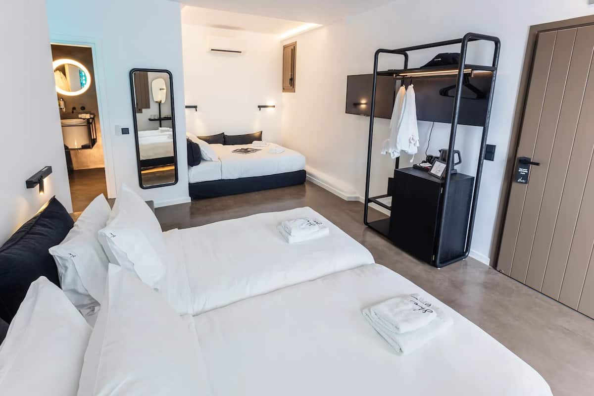 Una habitación de hotel con dos camas, un armario, un espejo y un pequeño escritorio con una lámpara.