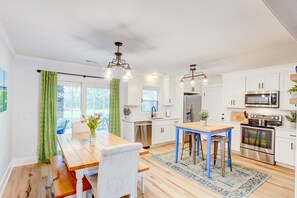 Une cuisine moderne avec des meubles blancs, des appareils en acier inoxydable et une table à manger en bois.